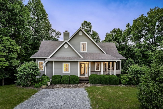 view of front of property with a front yard, covered porch, roof with shingles, and a chimney