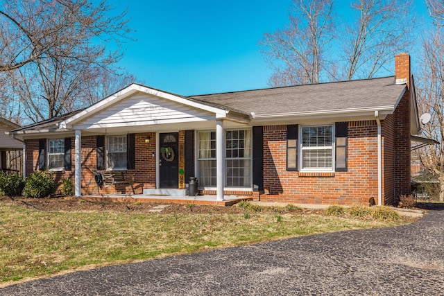 single story home featuring covered porch, brick siding, and a chimney