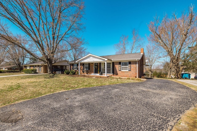 single story home featuring brick siding, a chimney, covered porch, driveway, and a front lawn