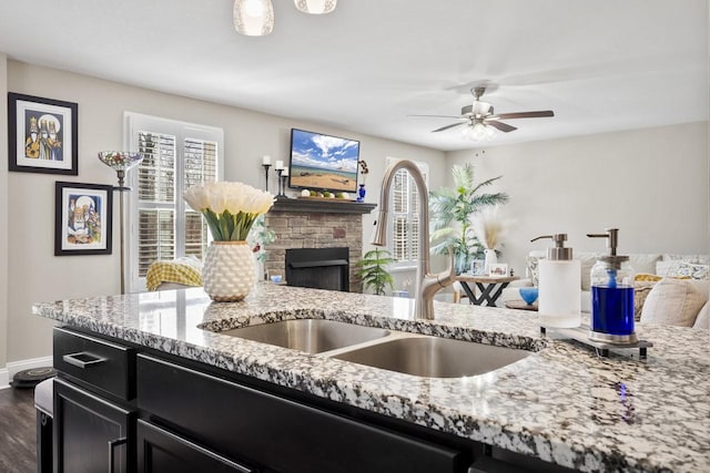 kitchen featuring light stone countertops, open floor plan, dark cabinets, a fireplace, and a sink