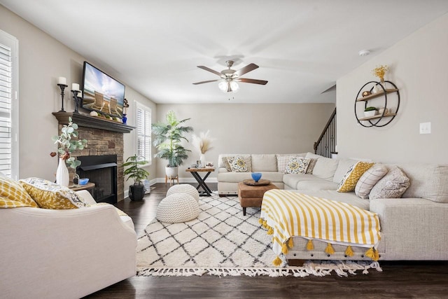 living area with a stone fireplace, wood finished floors, baseboards, and a ceiling fan