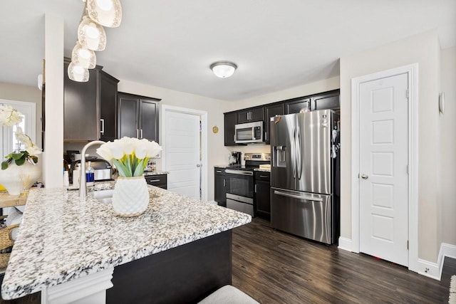 kitchen with light stone counters, a peninsula, appliances with stainless steel finishes, and dark wood finished floors