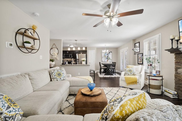 living area with ceiling fan with notable chandelier, baseboards, and dark wood-style flooring