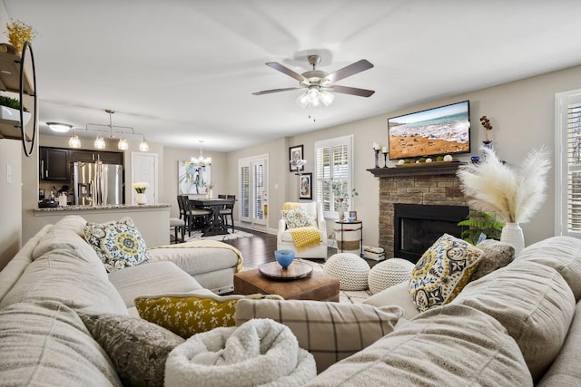 living room featuring wood finished floors, a fireplace, and ceiling fan with notable chandelier