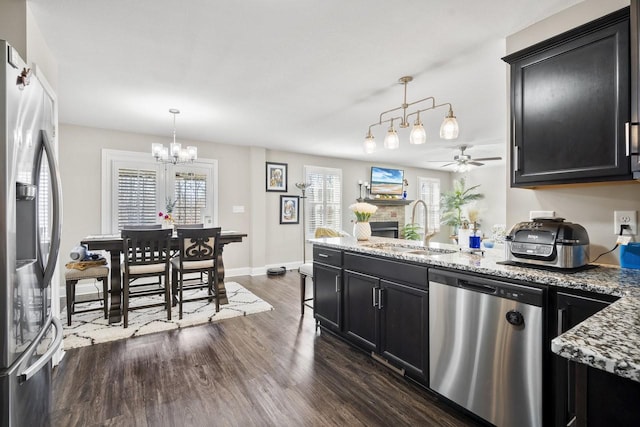 kitchen with a sink, dark wood finished floors, appliances with stainless steel finishes, a peninsula, and dark cabinets