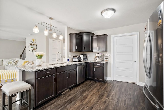 kitchen with a sink, dark wood finished floors, stainless steel appliances, a peninsula, and light stone countertops