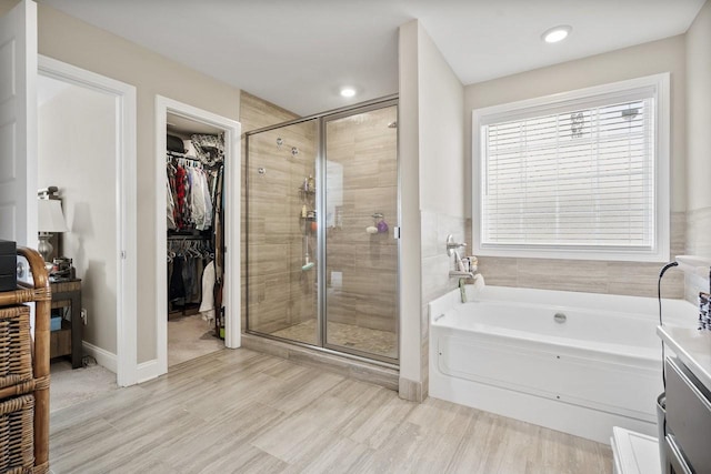 bathroom with a walk in closet, a shower stall, a garden tub, and wood finished floors