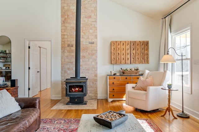 living room with a wood stove, baseboards, wood finished floors, and lofted ceiling