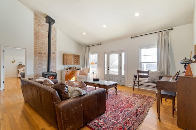 living room featuring a wood stove, light wood-type flooring, high vaulted ceiling, and recessed lighting