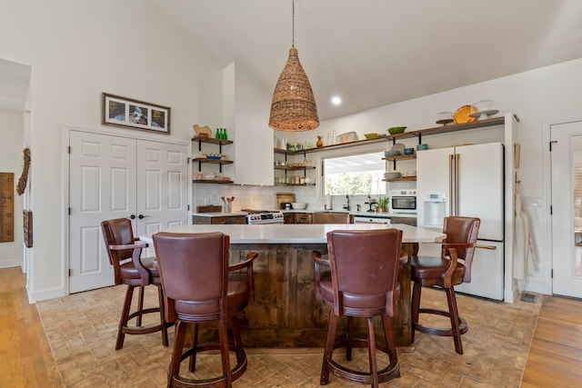 kitchen featuring white refrigerator with ice dispenser, a kitchen island, light countertops, open shelves, and stainless steel dishwasher