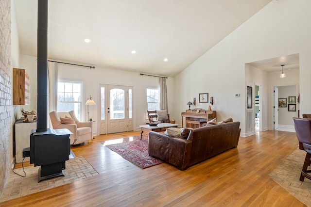 living area with baseboards, a wood stove, light wood-style floors, high vaulted ceiling, and recessed lighting