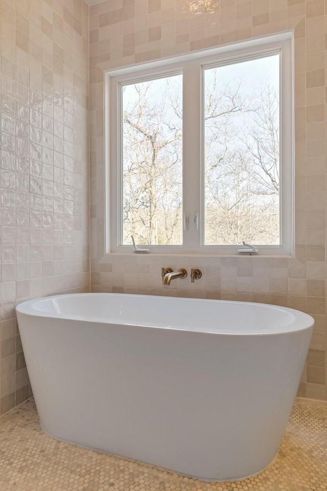 bathroom featuring a healthy amount of sunlight, a freestanding bath, and tile walls