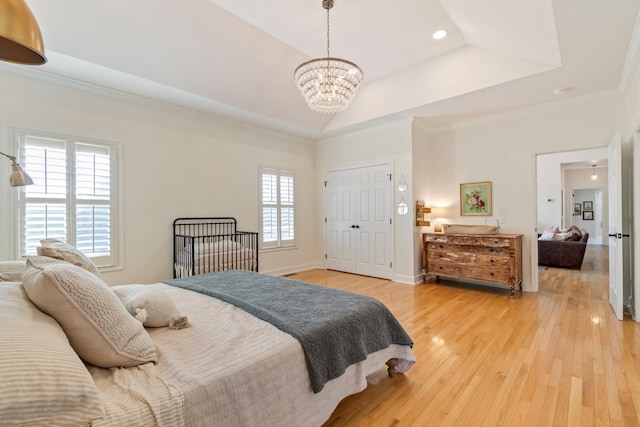 bedroom featuring baseboards, light wood-style flooring, ornamental molding, an inviting chandelier, and a tray ceiling