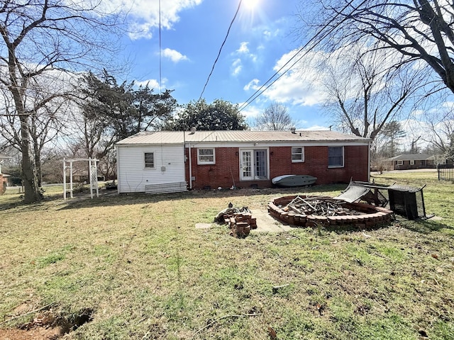 rear view of property featuring french doors, brick siding, a yard, metal roof, and a fire pit