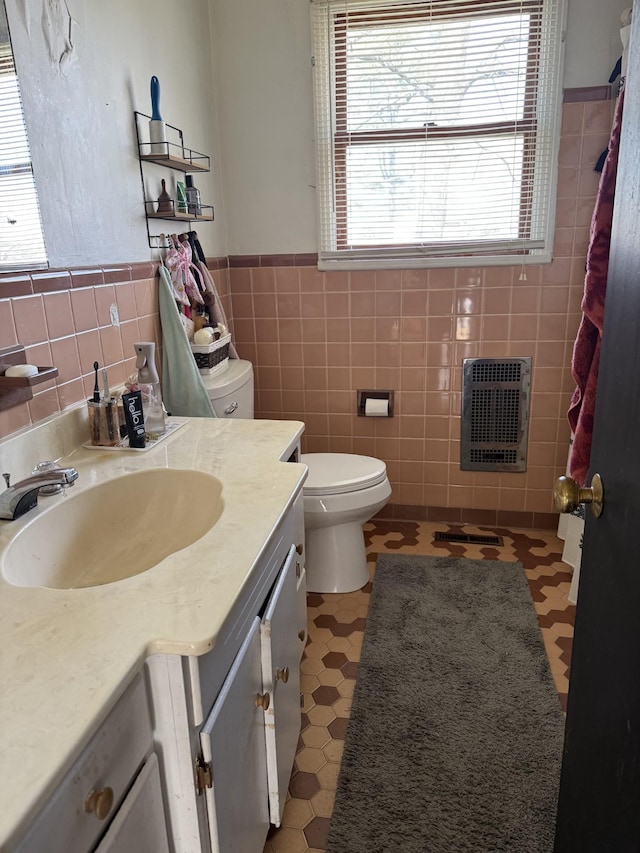 bathroom featuring tile walls, toilet, vanity, and heating unit