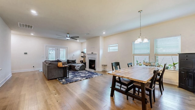 dining room with a healthy amount of sunlight, a warm lit fireplace, visible vents, and wood finished floors