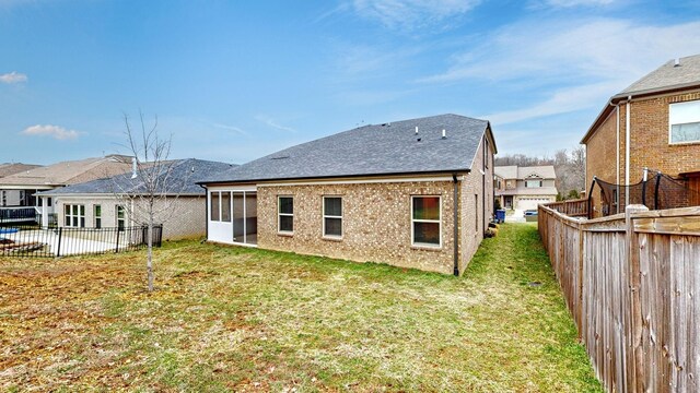 back of house with a sunroom, a fenced backyard, a lawn, and brick siding