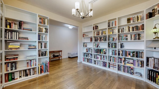 sitting room featuring wall of books, an inviting chandelier, and wood finished floors