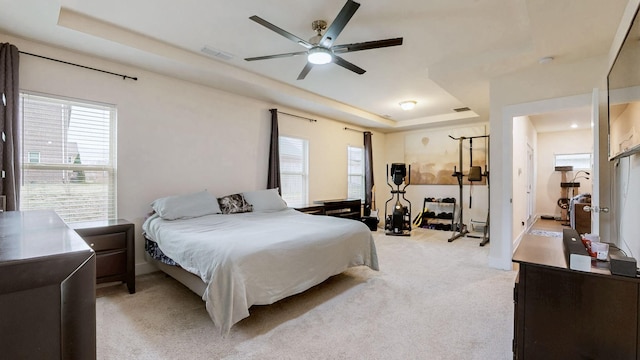 bedroom featuring light carpet, ceiling fan, visible vents, and a raised ceiling