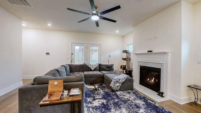 living area with ceiling fan, a premium fireplace, visible vents, and wood finished floors