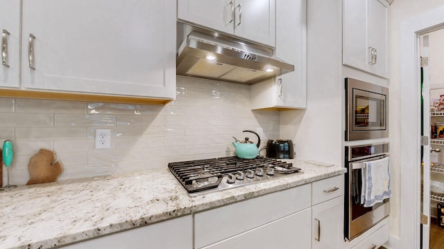 kitchen with stainless steel appliances, backsplash, white cabinets, and under cabinet range hood