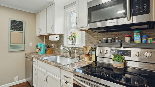 kitchen with a sink, white cabinets, appliances with stainless steel finishes, backsplash, and crown molding