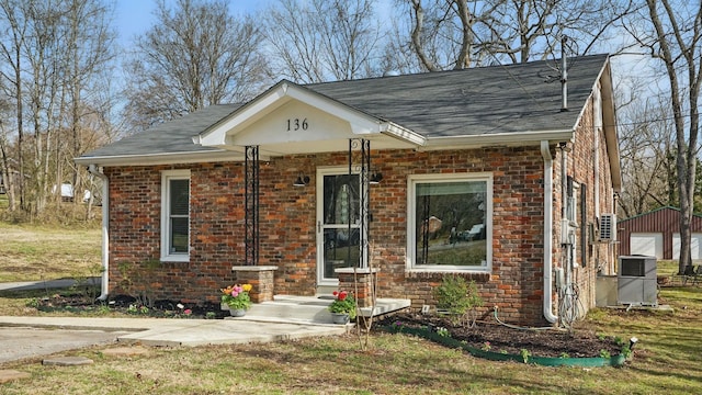 view of front of property with an outbuilding, brick siding, a shingled roof, and cooling unit