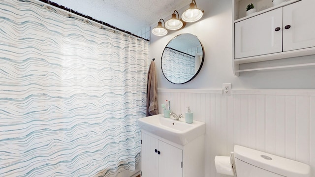 full bathroom with a wainscoted wall, a textured ceiling, vanity, and toilet