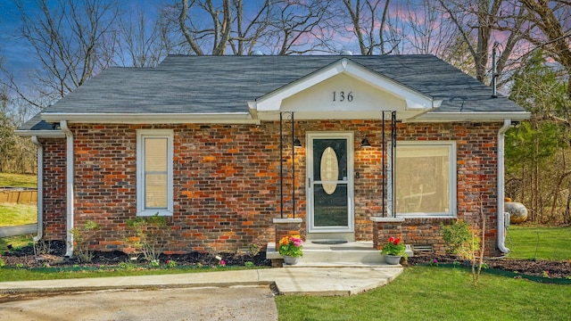 view of front of home featuring brick siding, a lawn, and roof with shingles