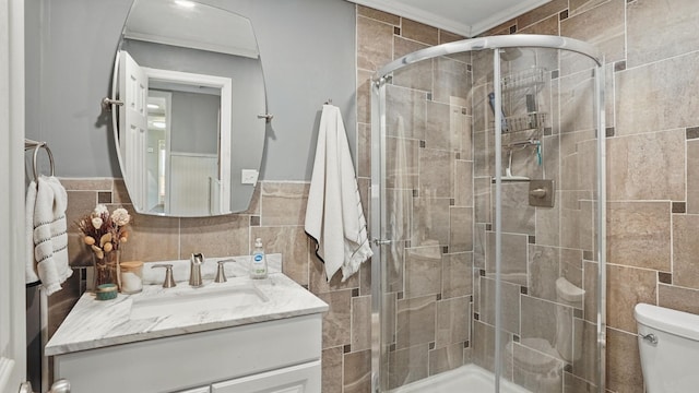 full bath with toilet, a stall shower, vanity, and tile walls