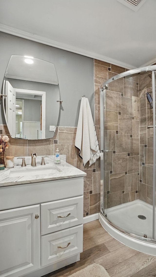 bathroom featuring a stall shower, ornamental molding, wood finished floors, vanity, and tile walls