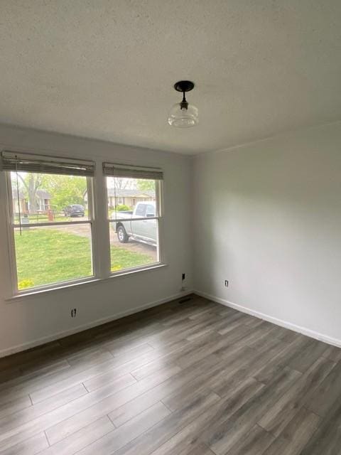 spare room with a textured ceiling, dark wood-type flooring, and baseboards