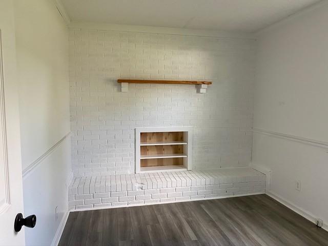 interior space with baseboards, wood finished floors, crown molding, built in shelves, and a fireplace