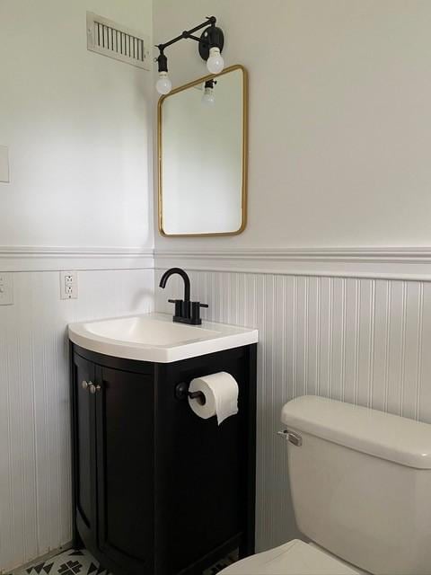 half bathroom featuring toilet, wainscoting, vanity, and visible vents