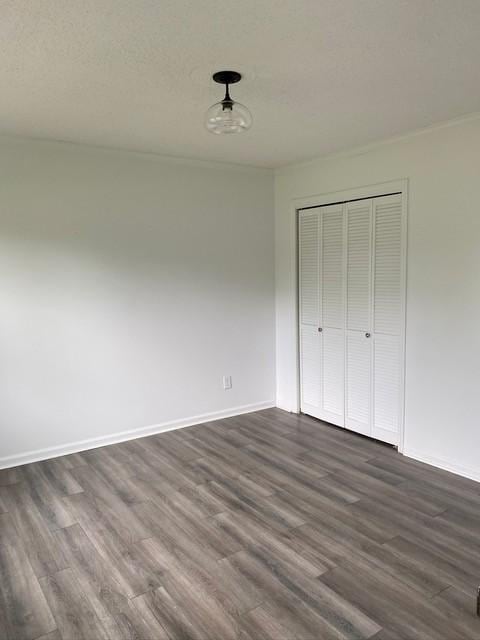 unfurnished bedroom with a textured ceiling, a closet, dark wood finished floors, and baseboards