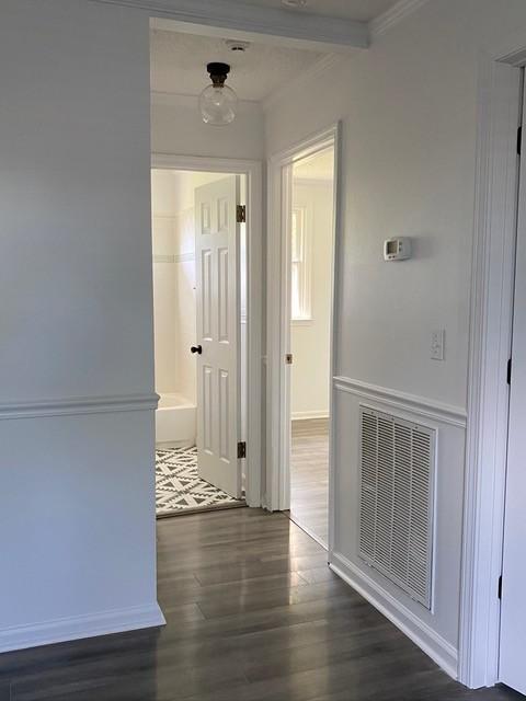 corridor featuring ornamental molding, visible vents, baseboards, and wood finished floors