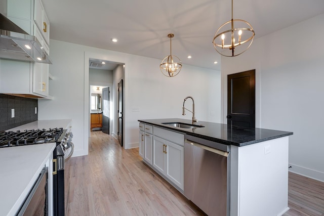 kitchen featuring stainless steel appliances, a sink, white cabinets, light wood-style floors, and tasteful backsplash