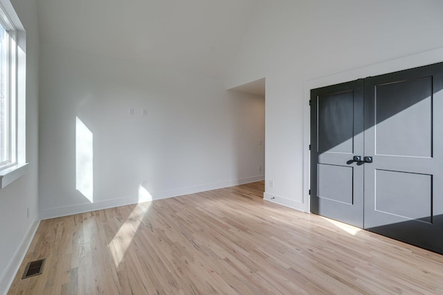 empty room featuring a high ceiling, visible vents, baseboards, and wood finished floors