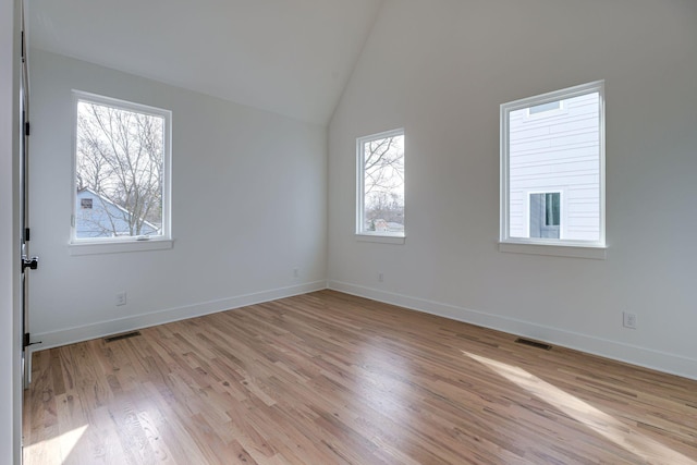 unfurnished room featuring visible vents, vaulted ceiling, light wood-style flooring, and baseboards