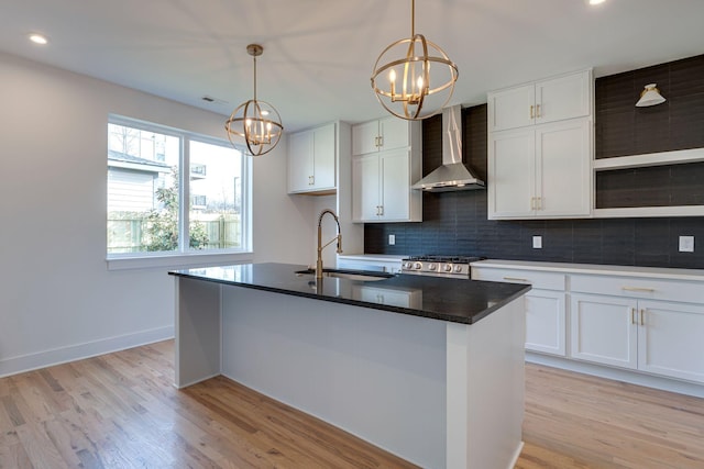 kitchen featuring wall chimney range hood, a sink, light wood-style flooring, and decorative backsplash