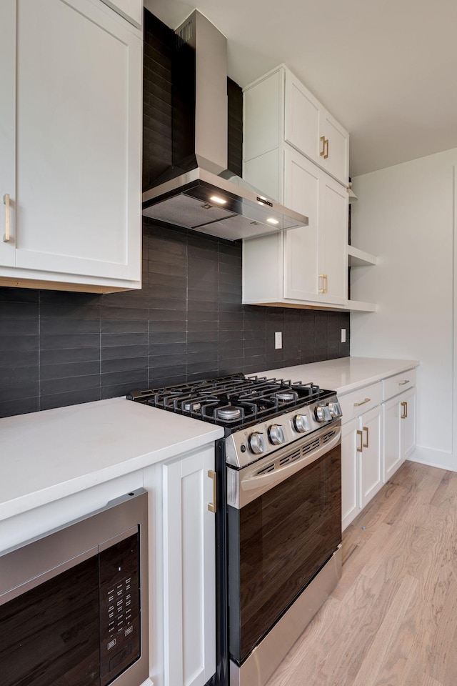 kitchen featuring white cabinets, decorative backsplash, wall chimney exhaust hood, light wood-style flooring, and appliances with stainless steel finishes