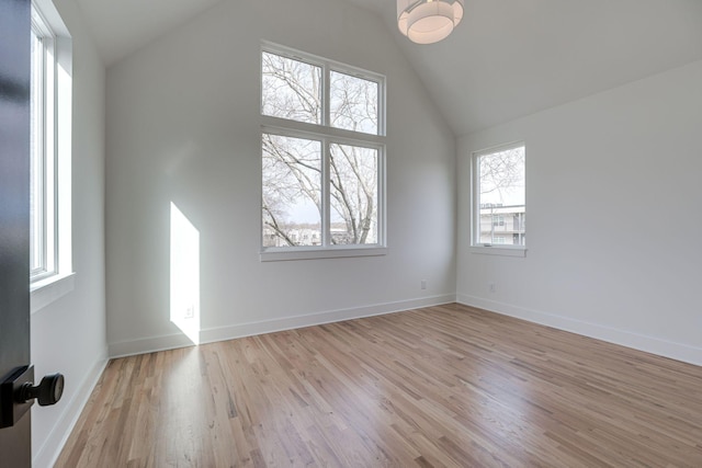 empty room featuring lofted ceiling, light wood-type flooring, and baseboards