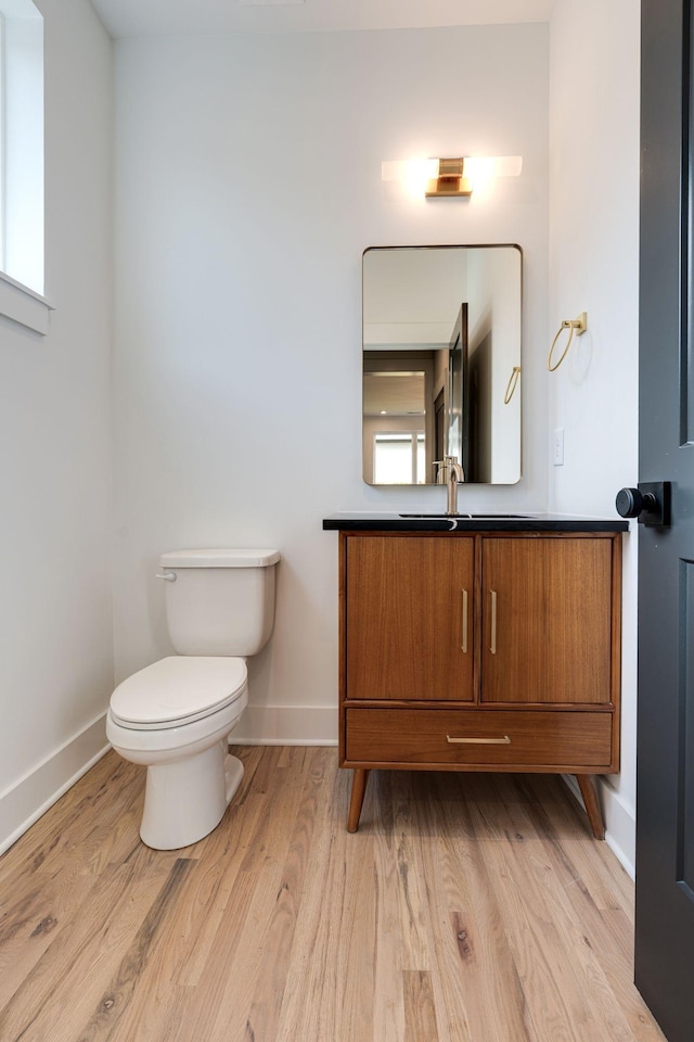 half bathroom with toilet, baseboards, wood finished floors, and vanity