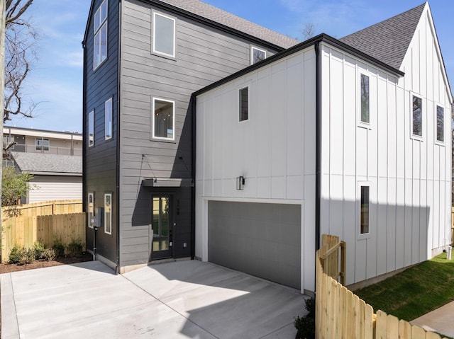rear view of property featuring fence, a garage, board and batten siding, roof with shingles, and driveway
