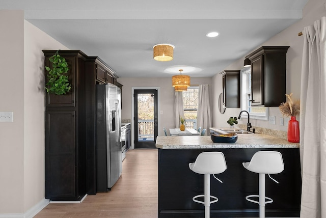 kitchen with light wood finished floors, light countertops, a sink, stainless steel fridge, and a peninsula