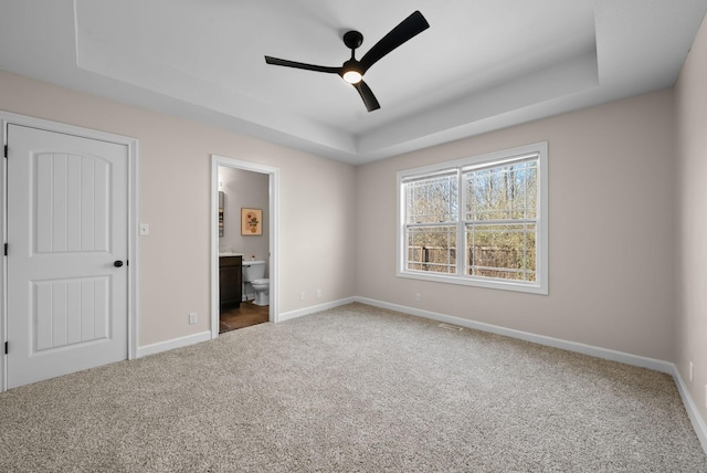 unfurnished bedroom with carpet, a tray ceiling, and baseboards