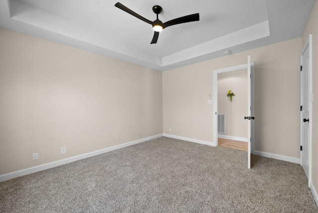 unfurnished bedroom with a tray ceiling, carpet flooring, visible vents, and baseboards