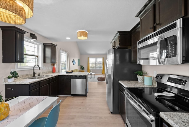 kitchen with lofted ceiling, appliances with stainless steel finishes, a sink, light wood-type flooring, and a peninsula