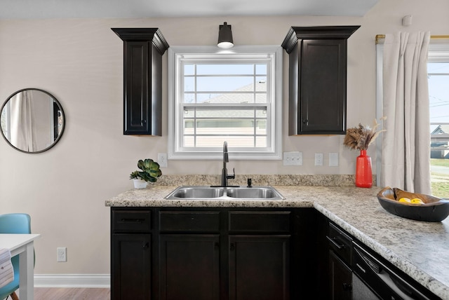 kitchen with light countertops, a sink, baseboards, and dark cabinetry