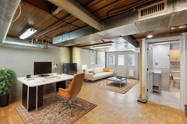 office space with parquet flooring, visible vents, and concrete block wall